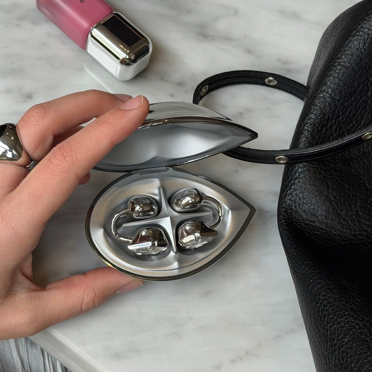 An open Electronic Gems case on a marble tabletop beside a bag and lip color.