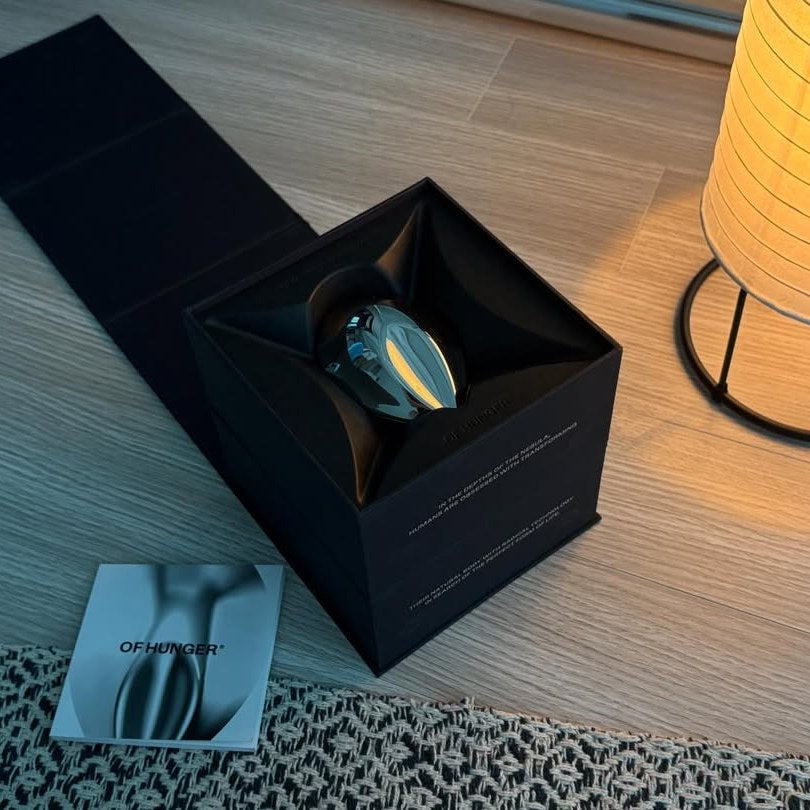 An open black OF HUNGER presentation box on a table beside a lamp.