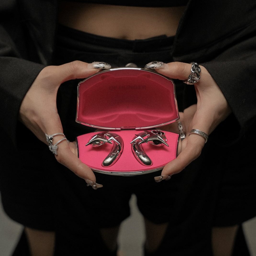 An open NEBULA charging case with a vivid pink interior held against a black outfit.