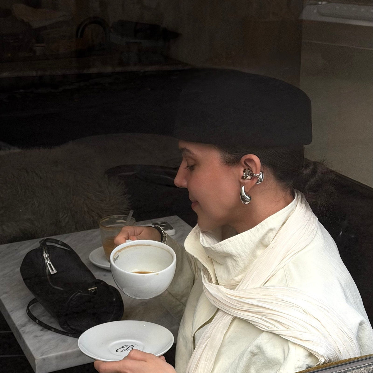 Electronic Gems worn with a black hat, cream scarf, and light-colored jacket at a cafe.
