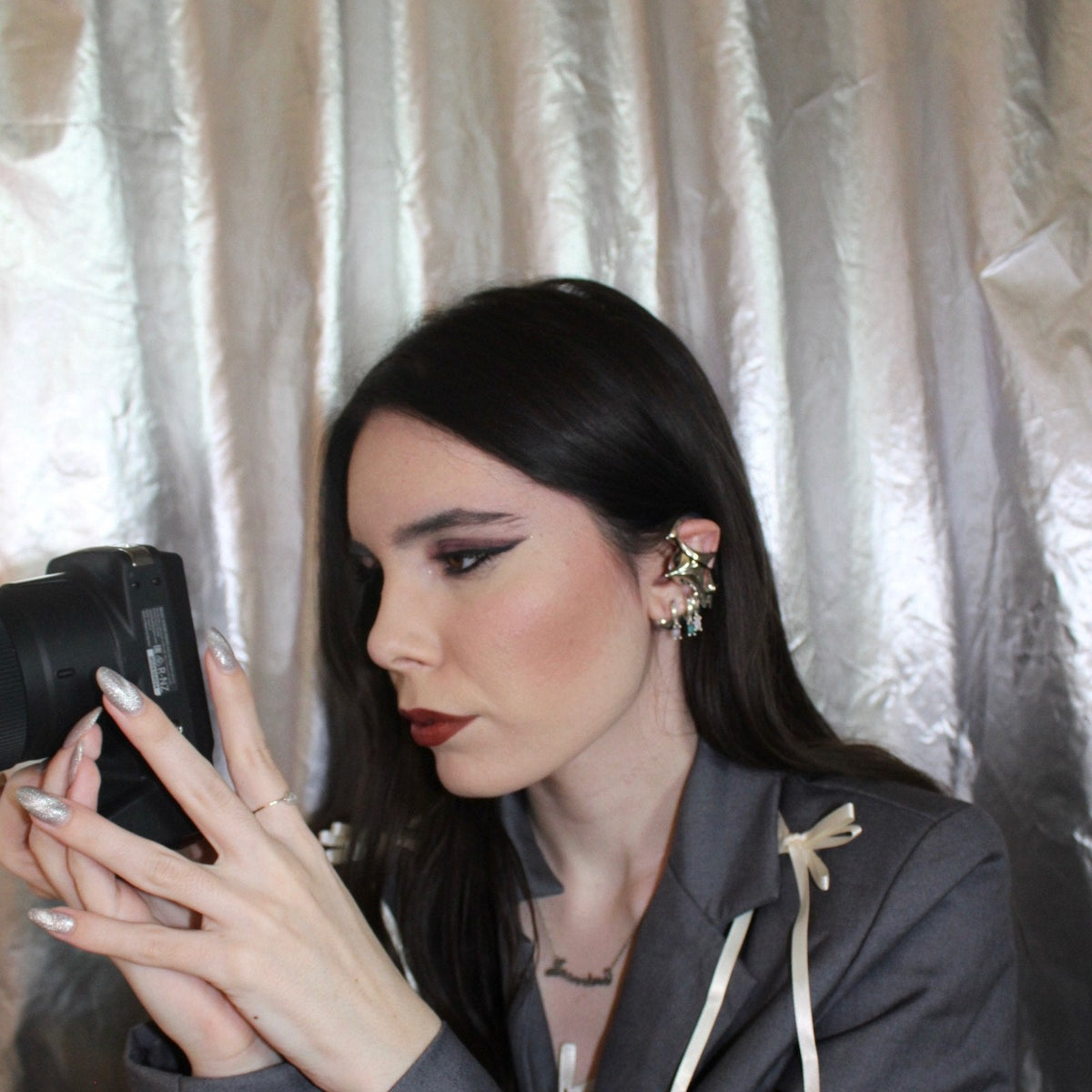 NEBULA ear-hook earphones worn while holding a camera, with a gray blouse and pale ribbons.