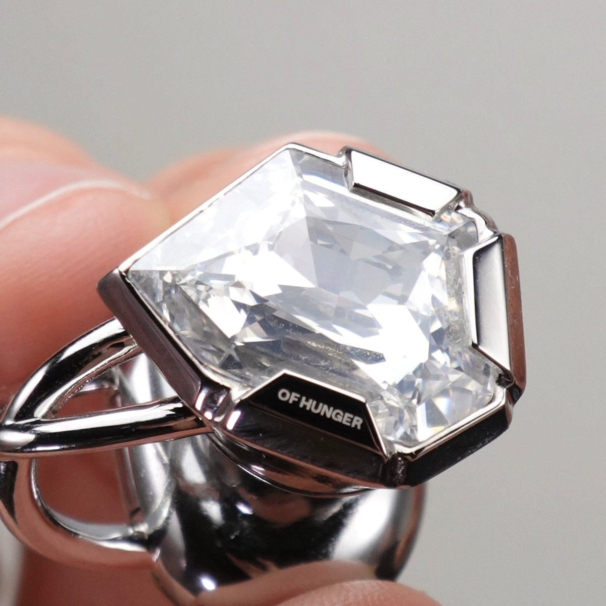 A close-up of an Electronic Gems ear clip held between fingertips, showing its faceted face and curved arms.